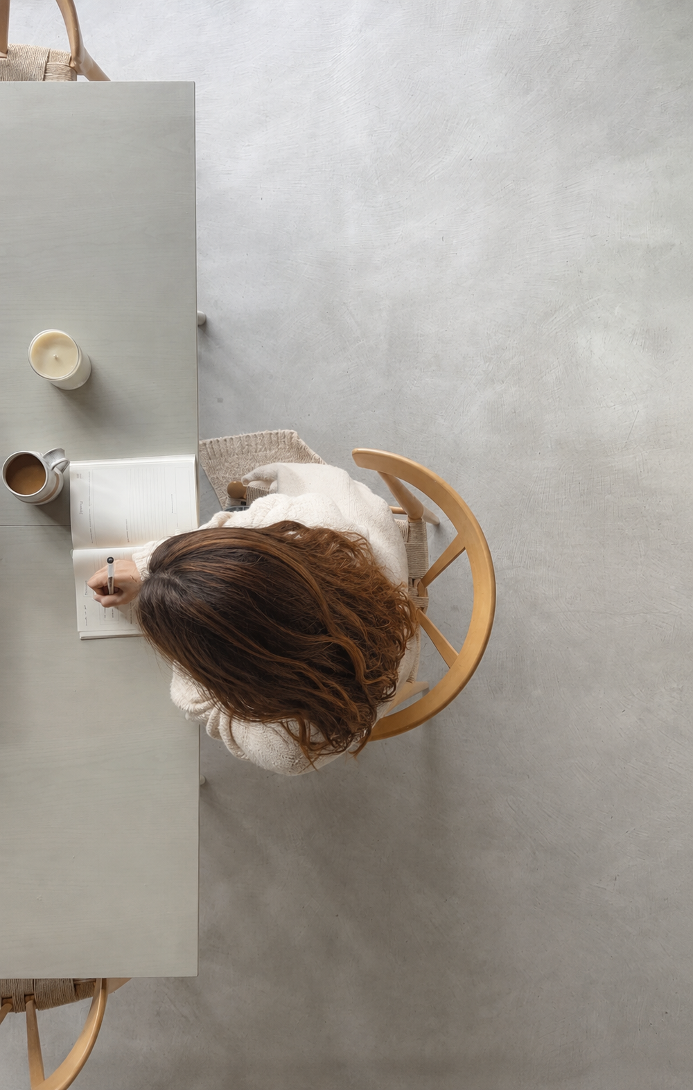 Vista cenital de una mujer escribiendo en un journal sobre una mesa clara